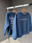 Two blue sweatshirts hanging on a rack with visible branding.